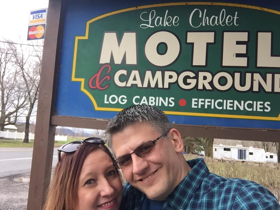 owners of lake chalet in front of welcome sign.